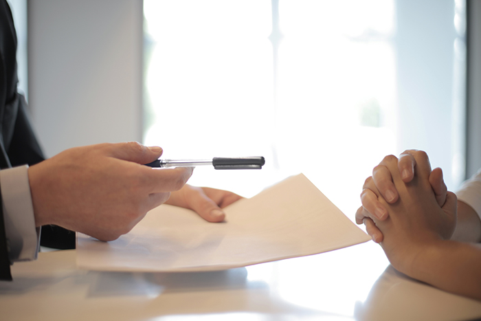 A hand passing a pen and document to another person’s hands