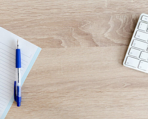 An image of a blank notebook and computer keyboard on a desk.