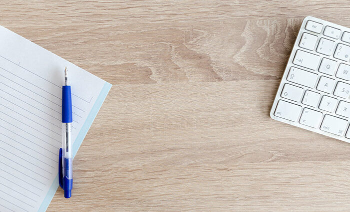 An image of a blank notebook and computer keyboard on a desk.